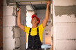 © Ольга Симонова - Construction worker at construction site measures the length of window opening and brick wall with tape measure. Cottage are made of porous concrete blocks, work clothes - jumpsuit and baseball cap