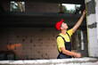 © Ольга Симонова - Construction worker at construction site measures the length of window opening and brick wall with tape measure. Cottage are made of porous concrete blocks, work clothes - jumpsuit and baseball cap
