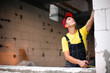 © Ольга Симонова - Construction worker at construction site measures the length of window opening and brick wall with tape measure. Cottage are made of porous concrete blocks, work clothes - jumpsuit and baseball cap