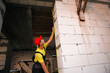 © Ольга Симонова - Construction worker at construction site measures the length of window opening and brick wall with tape measure. Cottage are made of porous concrete blocks, work clothes - jumpsuit and baseball cap