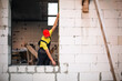 © Ольга Симонова - Construction worker at construction site measures the length of window opening and brick wall with tape measure. Cottage are made of porous concrete blocks, work clothes - jumpsuit and baseball cap