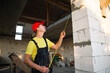 © Ольга Симонова - Construction worker at construction site measures the length of window opening and brick wall with tape measure. Cottage are made of porous concrete blocks, work clothes - jumpsuit and baseball cap