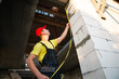 © Ольга Симонова - Construction worker at construction site measures the length of window opening and brick wall with tape measure. Cottage are made of porous concrete blocks, work clothes - jumpsuit and baseball cap