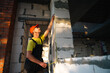 © Ольга Симонова - Construction worker at construction site measures the length of window opening and brick wall with tape measure. Cottage are made of porous concrete blocks, work clothes - jumpsuit and baseball cap