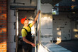 © Ольга Симонова - Construction worker at construction site measures the length of window opening and brick wall with tape measure. Cottage are made of porous concrete blocks, work clothes - jumpsuit and baseball cap