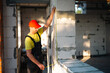© Ольга Симонова - Construction worker at construction site measures the length of window opening and brick wall with tape measure. Cottage are made of porous concrete blocks, work clothes - jumpsuit and baseball cap