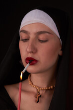 Portrait Of A Bad Young Nun Lights Up A Cirarette Using A Church Candle. The Act Of Desecration And Blasphemy.