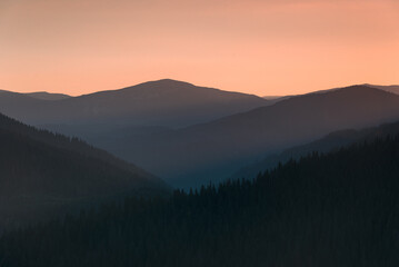 Wall Mural - Amazing landscape of mountains at sunrise. View of orange sky and hills covered forest at mist.