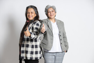 Wall Mural - Portrait of a two confident mature senior indian businesswomen in a suit do thumbs up isolated on white background. successful gray-haired 60s asian lady executives manager standing, copy space.