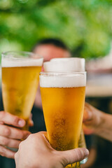 Wall Mural - Close-up view of a three glass of beer in hand. Beer glasses clinking at outdoor bar or pub