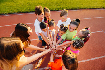 Wall Mural - A large group of children, boys and girls, stand together in a circle and fold their hands, tuning up and raising team spirit before the game at the stadium during sunset. A healthy lifestyle.