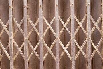 Close-up of old metal curtains with cross and rust; old sliding metal door, closed and abandoned storefront, metallic gate background