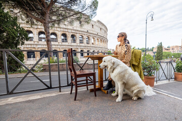 Wall Mural - Woman sitting with her dog at outdoor cafe near coliseum, the most famous landmark in Rome. Concept of italian lifestyle with pets and traveling Italy