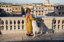 Woman Enjoys Beautiful Cityscape Of Old Rome City, Standing Back With Her Dog On The Top Of Spanish Steps In The Morning. Concept Of Italian Lifestyle And Travel