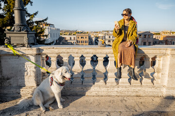 Wall Mural - Woman enjoys beautiful cityscape of old Rome city, standing back with her dog on the top of Spanish steps in the morning. Concept of italian lifestyle and travel