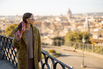 Wall Mural - Woman enjoying beautiful morning cityscape of Rome, walking in Villa Borghese Park. Old fashioned woman wearing coat with colorful shawl in hair. Concept of italian lifestyle and travel