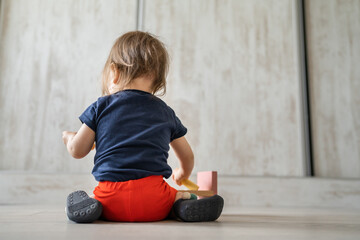 One girl toddler female child playing alone at home with wooden creative educational toys copy space back view