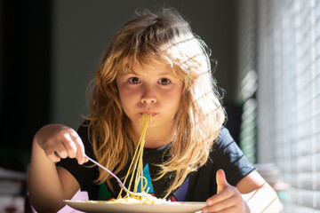 Cute little kid eating spaghetti pasta at home. Close up portrait of funny kid eating. Little boy having breakfast in the kitchen.