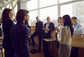 Wall Mural - Team of business people communicating with each other. Group of happy positive young men and women standing in modern office, talking, sharing impressions after corporate meeting or training session