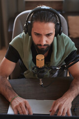 Wall Mural - Vertical high angle portrait of serious Middle Eastern male influencer sitting at desk checking something on laptop