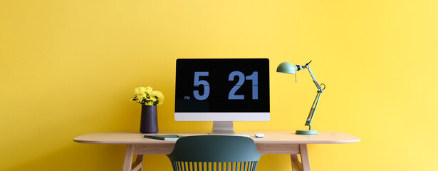 Workplace with modern computer and lamp near yellow wall
