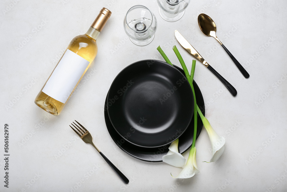 Beautiful table setting with calla lilies and bottle of wine on light background