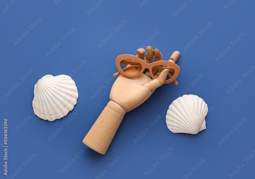 Wooden hand with sunglasses and seashells on blue background