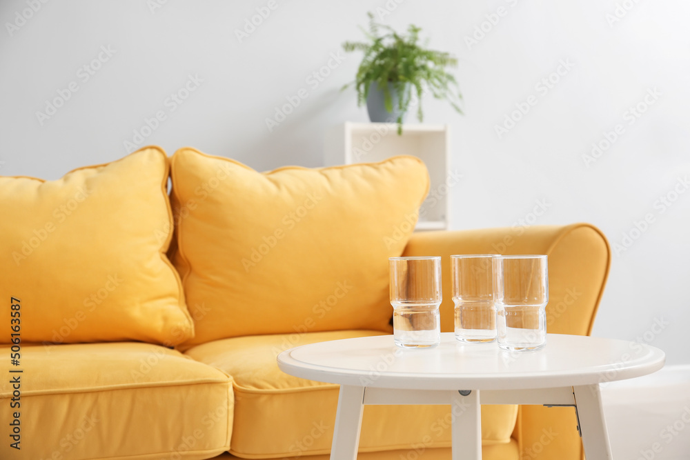 Glasses on table near sofa in living room, closeup
