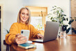 © baranq - Cheerful mature woman wearing glasses using smartphone working at home office