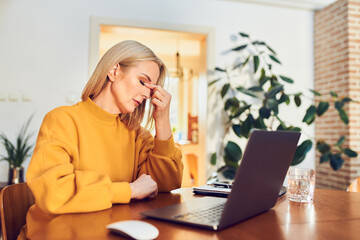 Mature woman having headache while working at home office