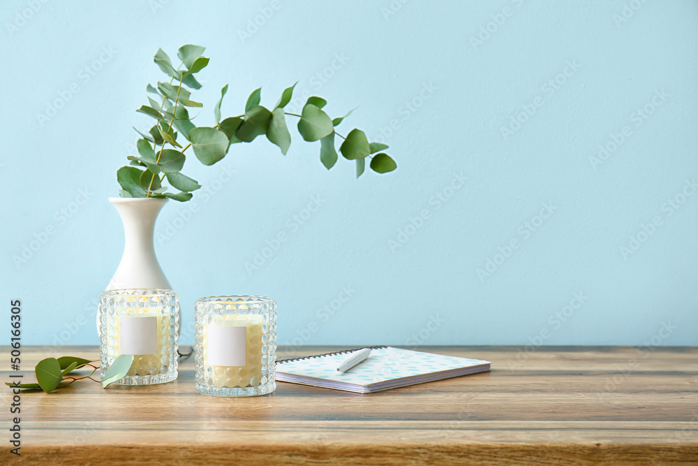Holders with burning candles and eucalyptus branches on wooden table