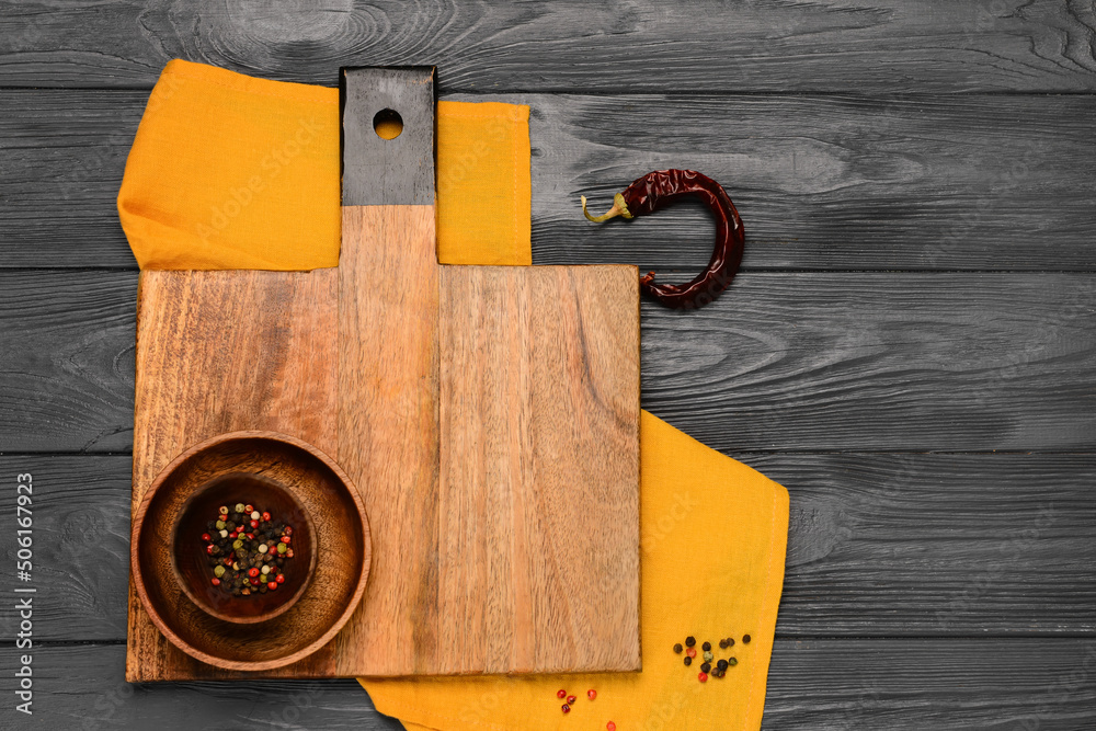 Cutting board and bowl with peppercorn on black wooden background