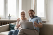 © fizkes - Happy excited mature couple using laptop at home, making video call from sofa, talking, laughing, smiling at screen. Cheerful senior husband and wife using online app, getting good news