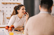 © dusanpetkovic1 - A woman eating apple in kitchen at home and smiling at boyfriend.