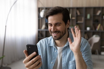 Wall Mural - hello. happy millennial man wave hand hi look at smartphone screen start talk by video call with fri