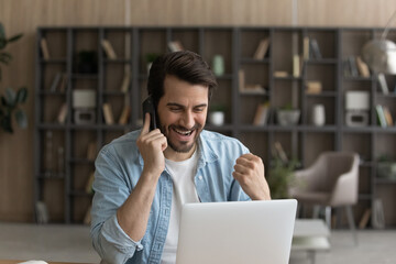 Wall Mural - business win. overjoyed millennial businessman working from home sit by laptop discuss perfect sales