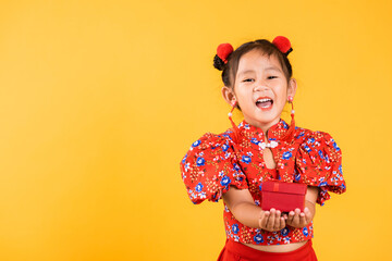 Chinese New Year. Happy Asian Chinese little girl smile wearing red cheongsam holding gift box, Portrait children in traditional dress hold, studio short isolated on yellow background