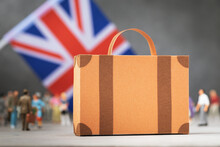 Cardboard Suitcase, Plastic Toy People And A Flag On An Abstract Background, A Concept On The Theme Of Moving Or Immigrating To Britain