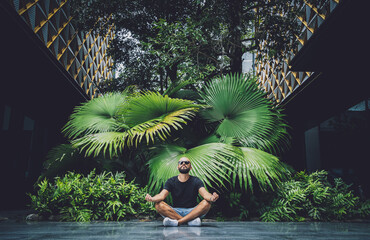 Young man meditating yoga at beautiful green leaves background in jungle