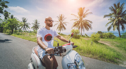 Wall Mural - Stylish young man rides a motorbike on the road near the sea and palm trees