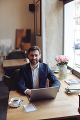 Wall Mural - Caucasian handsome man smiling, sitting at table with laptop in cafe. Business. Vertical. Portrait.