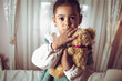 Little multiracial girl holding her teddy bear, looking scared