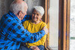 © PoppyPix - senior couple hugging in front of the window medium shot indoor senior people support concept. High quality photo