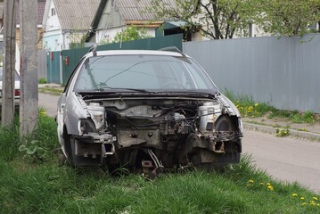 one gray black disassembled car stands in the green grass near the road on the street