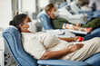 canvas print picture Side view portrait of people wearing masks while giving blood in row at medical donation center