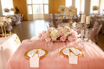 table decoration with pink tablecloth, crystal candlesticks with candles and white pink flowers in restaurant . stylish wedding day. setting table with gold plate, fork and knife