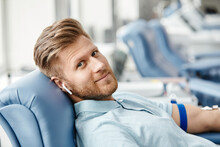 Portrait Of Smiling Young Man Donating Blood While Lying In Comfortable Chair At Med Center And Looking At Camera