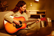 © Seventyfour - Portrait of attractive young adult Caucasian woman with long curly hair playing guitar in evening at home