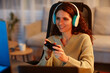 © Seventyfour - Cheerful young adult Caucasian woman wearing headphones playing video game using controller in living room late in evening