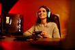 © Seventyfour - Modern young adult Caucasian woman playing racing or shooter video game using console in living room at night